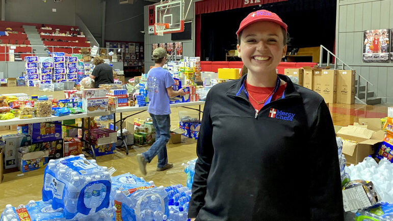 Molly MacDonald stands in front of a stack of donated bottled water packages in the Sharkey Issaquena Academy gym in Rolling Fork, Mississippi, on March 27, 2023.