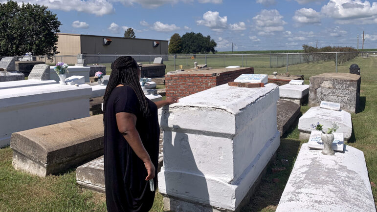 Marla Dickerson places her hand on the grave of her great-great-grandfather, Robert Taylor, at the Revilletown cemetery in Plaquemine, Louisiana, on September 6, 2023.