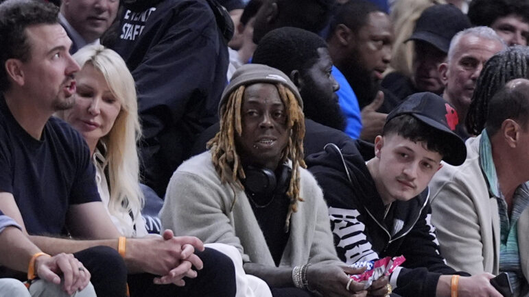 Rapper Lil Wayne, center, watches during the second half of an NBA basketball game between the Miami Heat and the Golden State Warriors, Tuesday, March 26, 2024, in Miami.