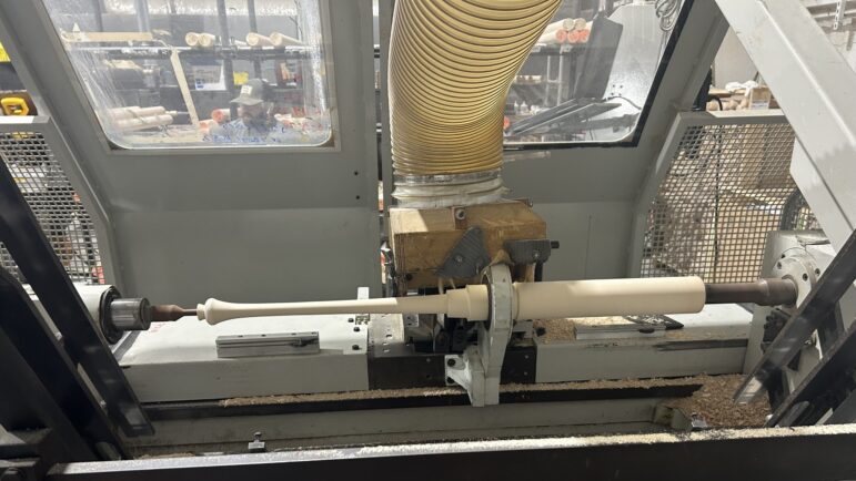 A machine shapes the bat by shaving off layers of wood.